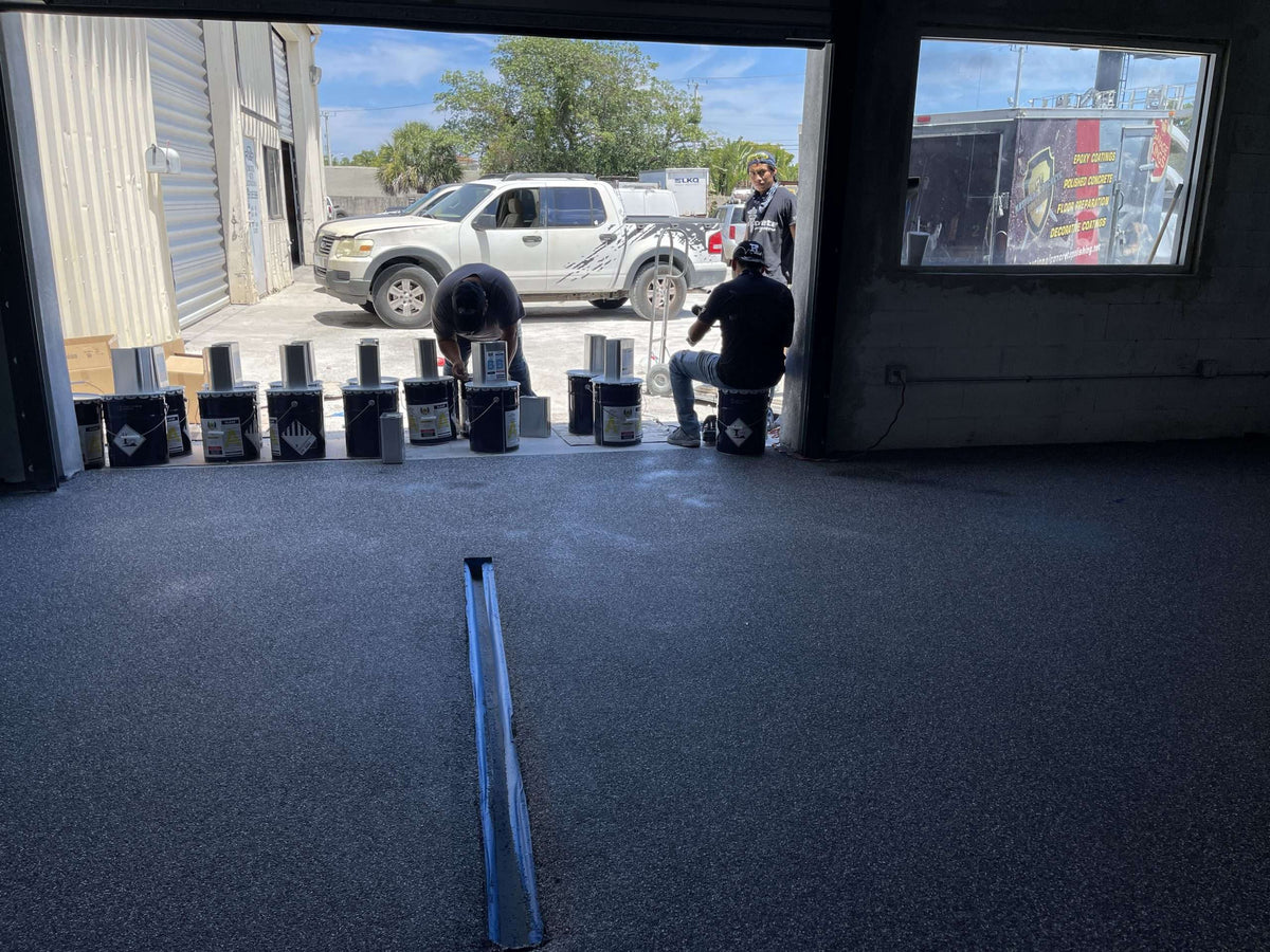 An image showing flooring technicians preparing a large garage for epoxy installation.
