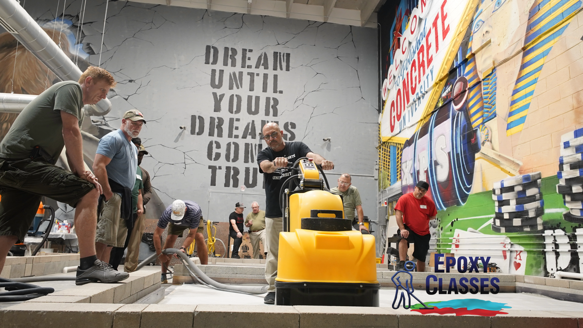 An epoxy resin contractor teaching students how to operate a flooring grinder in a warehouse.